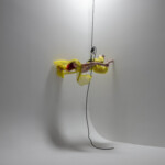 Sonsherée Giles suspended by rope and harness in the air, dancing in yellow clothing.