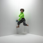 Saharla Vetch dancing in a corner with a swinging metal coffee mug, wearing a green top and black pants.