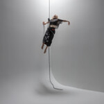 Mary Starr Hope suspended by rope and harness in the air, dancing in black clothing.