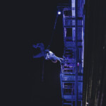 B Dean dancing on a fire escape suspended by rope and harness