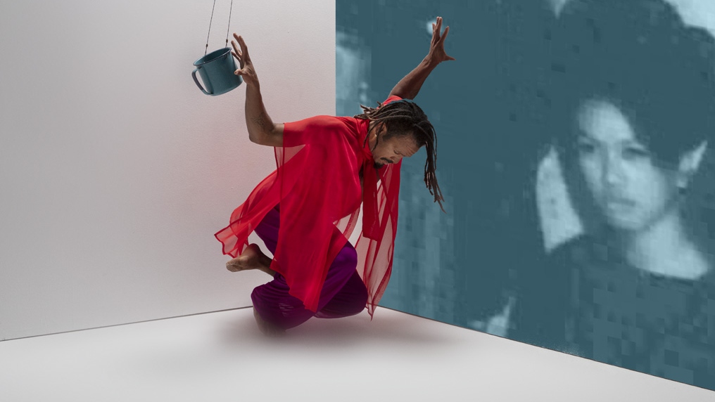 Gabriele Christian dancing in a corner with a swinging metal coffee mug, wearing a red top and black pants.