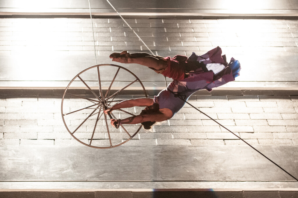 Esther Wrobel flipping in the air with a metal umbrella, suspended via rope and harness equipment.